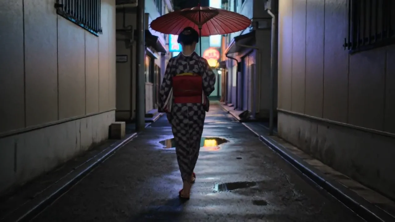 雨上がりの夜の路地裏で、赤い和傘を差した着物の若い女性がネオンの映る水たまりを踏んで歩き、水面に波紋が広がる動画